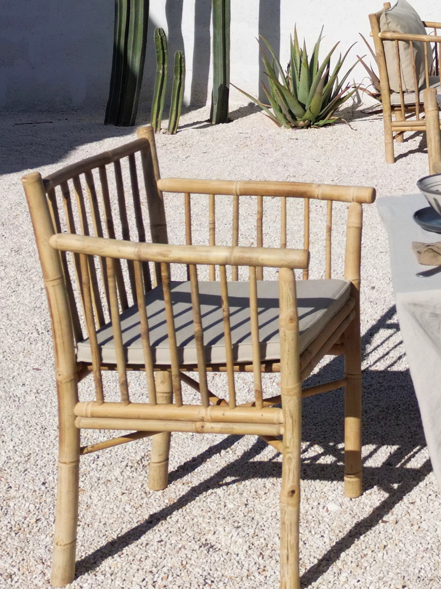 Tine K Outdoor Bamboo Dining Chair With Armrest - Set of 4, a natural bamboo dining chair featuring a light, warm-toned bamboo frame with vertical slatted backrest and armrests, complemented by a soft light grey fabric seat cushion. This coastal-inspired outdoor armchair is perfect for creating a relaxed boho dining area on patios, gardens, or terraces.