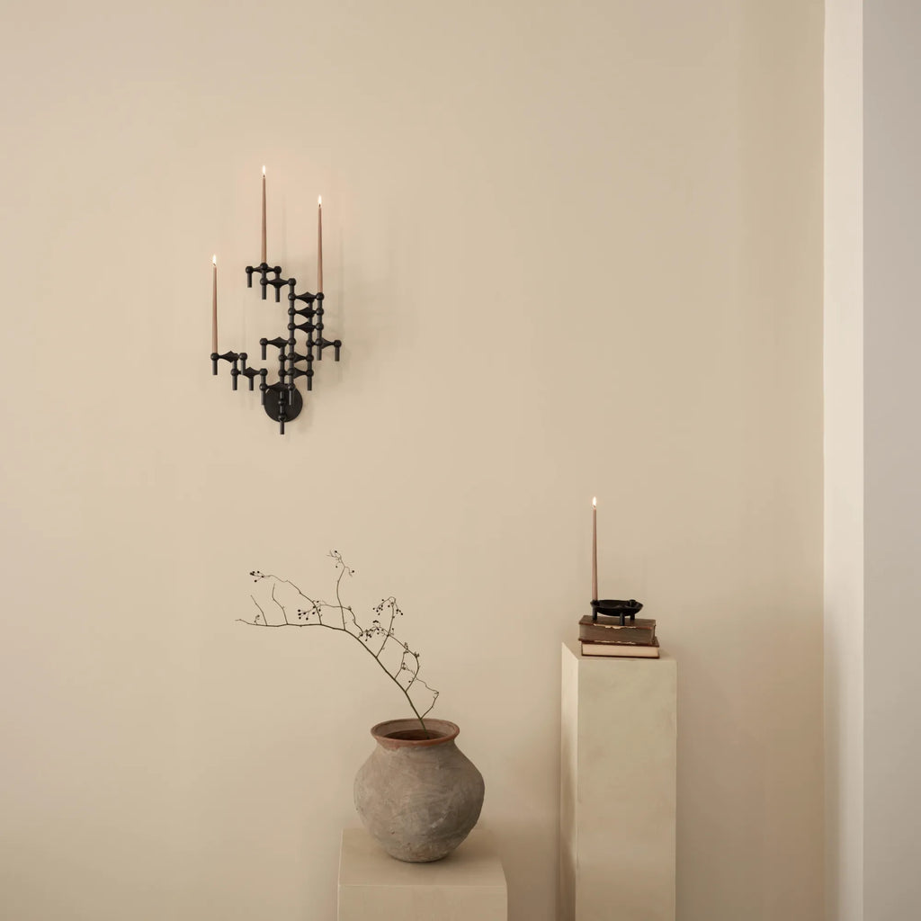 Stoff Nagel Wall Hanger Candle Holder - Black - Configuration 3, a striking mid-century modern wall-mounted candle holder crafted from matte black metal in a modular, sculptural design with interlocking geometric shapes. This brutalist-inspired piece holds three natural beige taper candles, creating a warm, ambient glow. Perfect as industrial chic wall decor for a living room, entryway, or contemporary dining space.