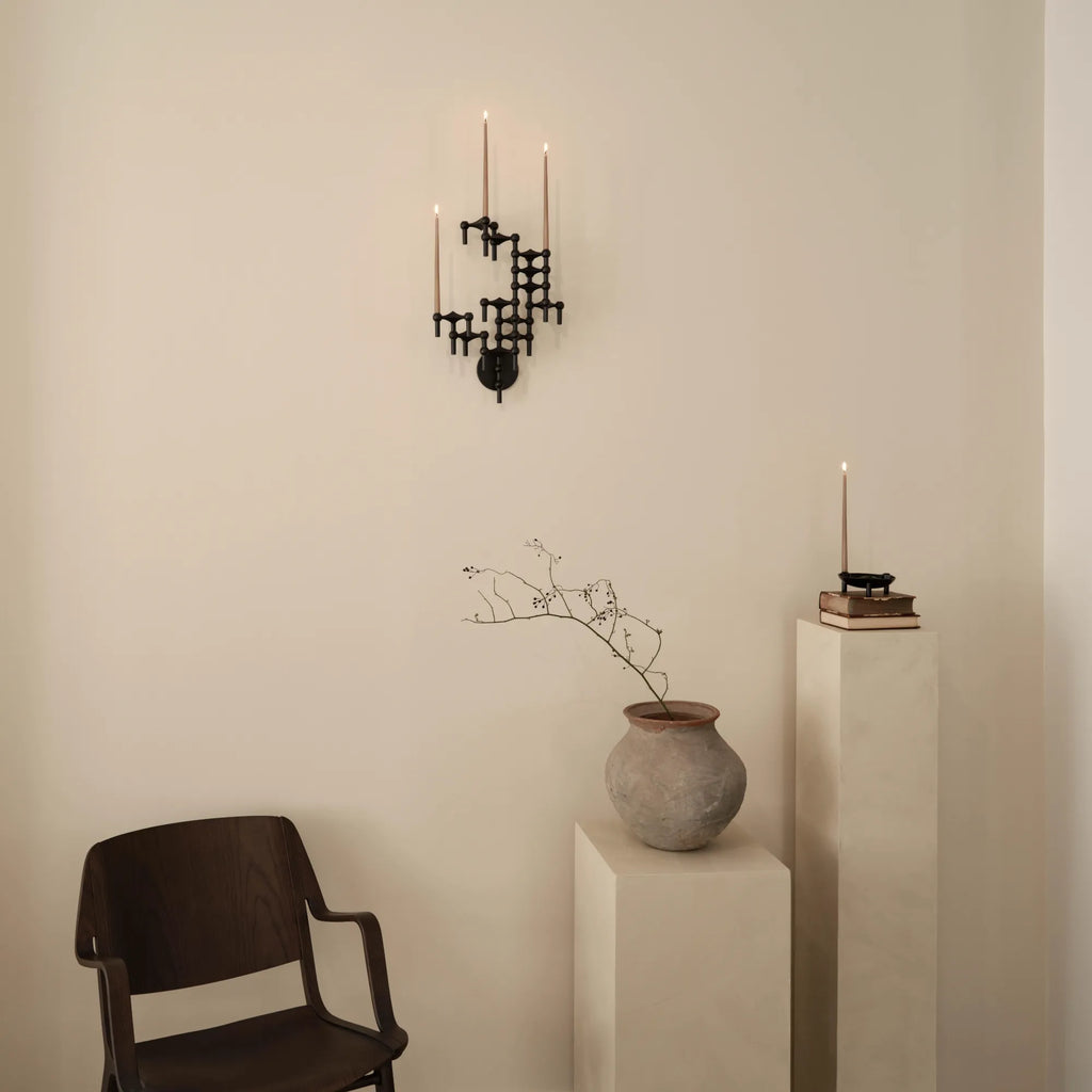 Stoff Nagel Wall Hanger Candle Holder - Black - Configuration 3, a striking mid-century modern wall-mounted candelabra crafted from matte black metal with a modular, geometric design. This sculptural wall art piece features interlocking hexagonal shapes, holding three tall taupe taper candles, creating an industrial chic aesthetic. Perfect as a designer wall decor accent for living rooms, entryways, or contemporary brutalist interiors.