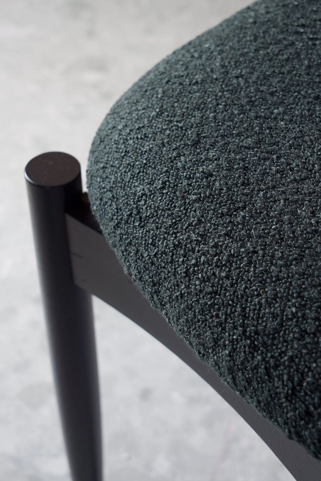 TAMO Kemi Chair, a modern minimalist dining chair featuring a deep dark green textured bouclé fabric upholstery on a subtly curved seat, supported by a sleek, dark-stained solid wood frame. This elegant and comfortable chair is ideal for contemporary dining rooms or as a stylish accent piece in Scandinavian-inspired living spaces.