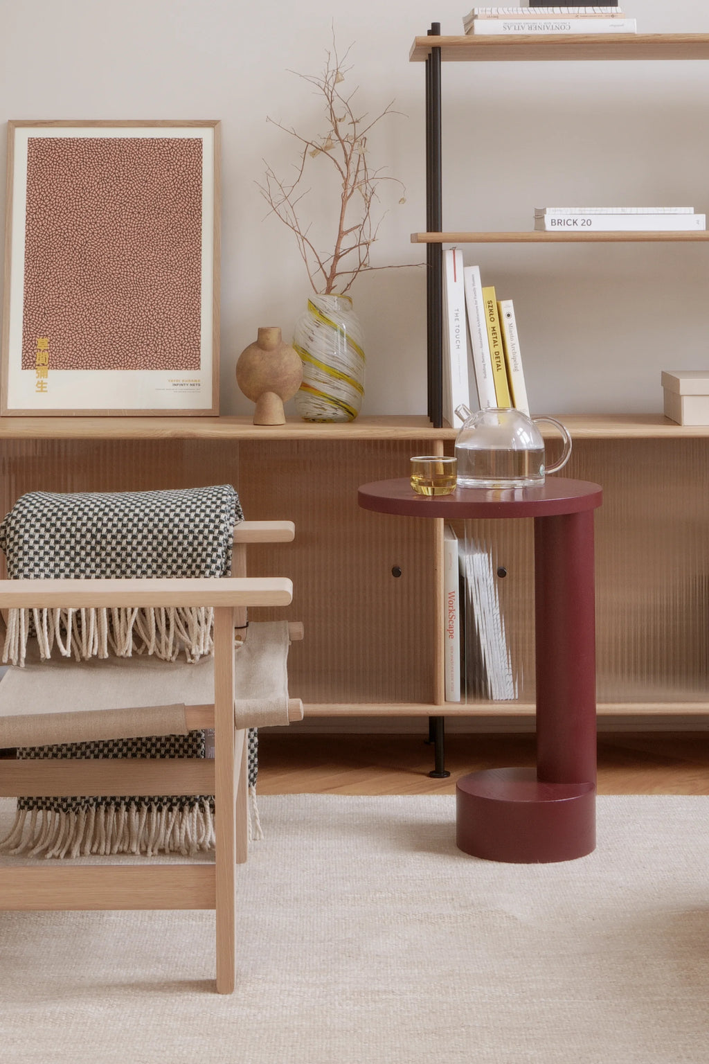 TAMO Bold Side Table, a premium matte oxblood red C-shaped table with cylindrical base and top, styled with a glass teapot and cup. Ideal for modern living spaces.