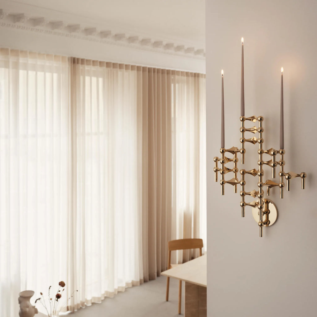 Stoff Nagel Wall Hanger Candle Holder - Solid Brass - Configuration 2, a striking modular sculptural wall sconce crafted from polished solid brass, featuring interconnected spheres and rods that create a dynamic, Brutalist-inspired geometric form. This mid-century modern wall candle holder, shown with three slender grey taper candles, is perfect for adding industrial chic wall decor to a living room, entryway, or dining area.