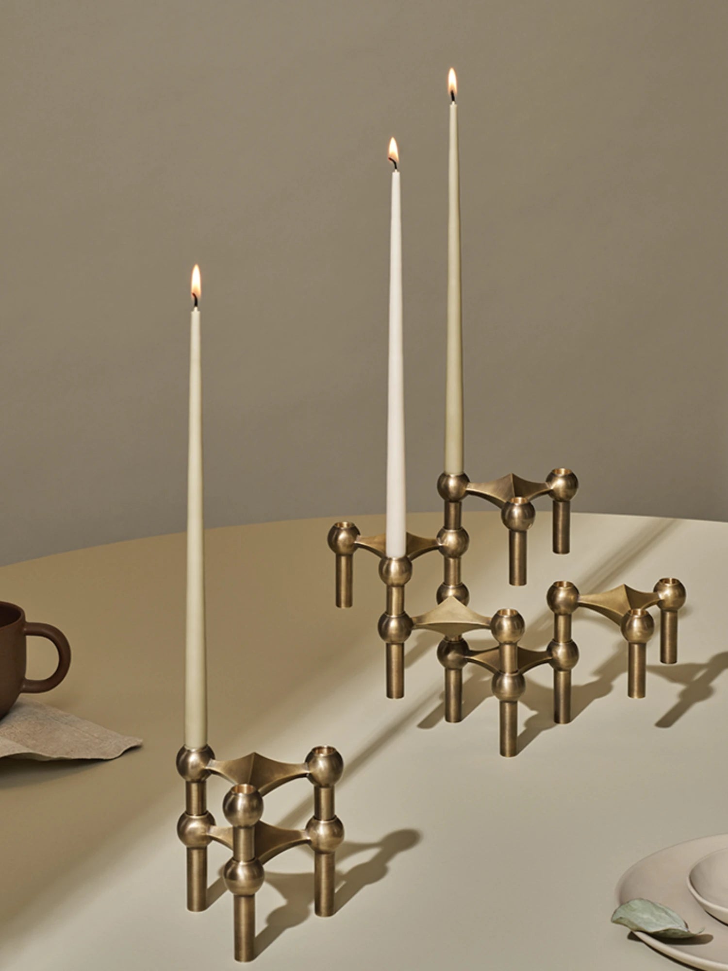 Bronze stoff nagel candle holder with three lit taper candles on a neutral dining table setting