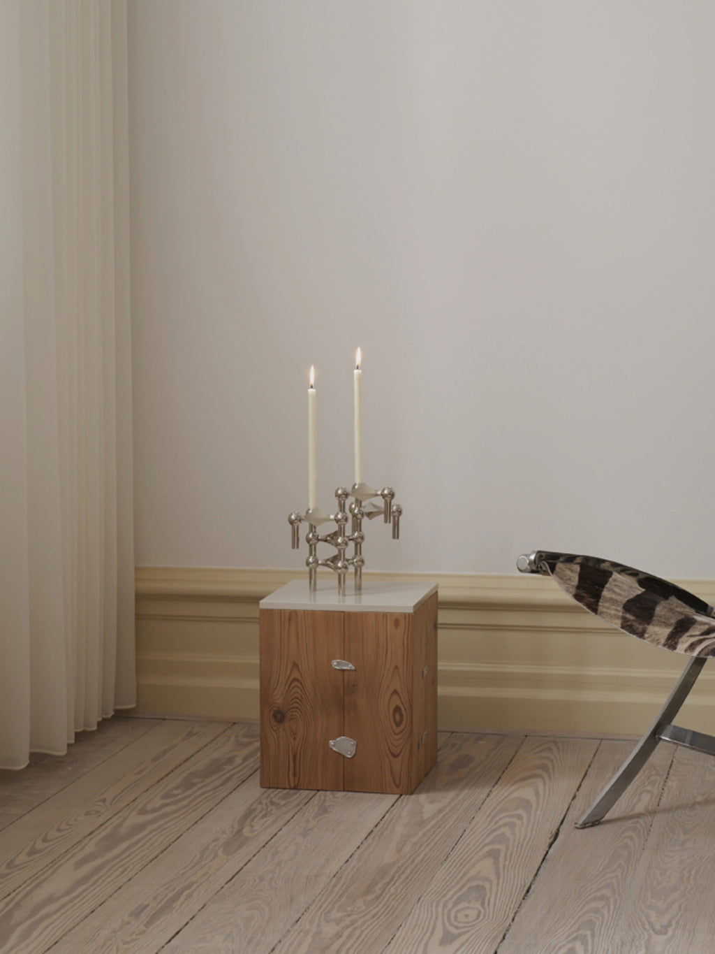 white stoff nagel candles on top a designer wooden side table in a minimalistic scandinavian designer furniture setting.