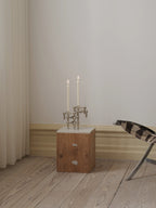 white stoff nagel candles on top a designer wooden side table in a minimalistic scandinavian designer furniture setting.