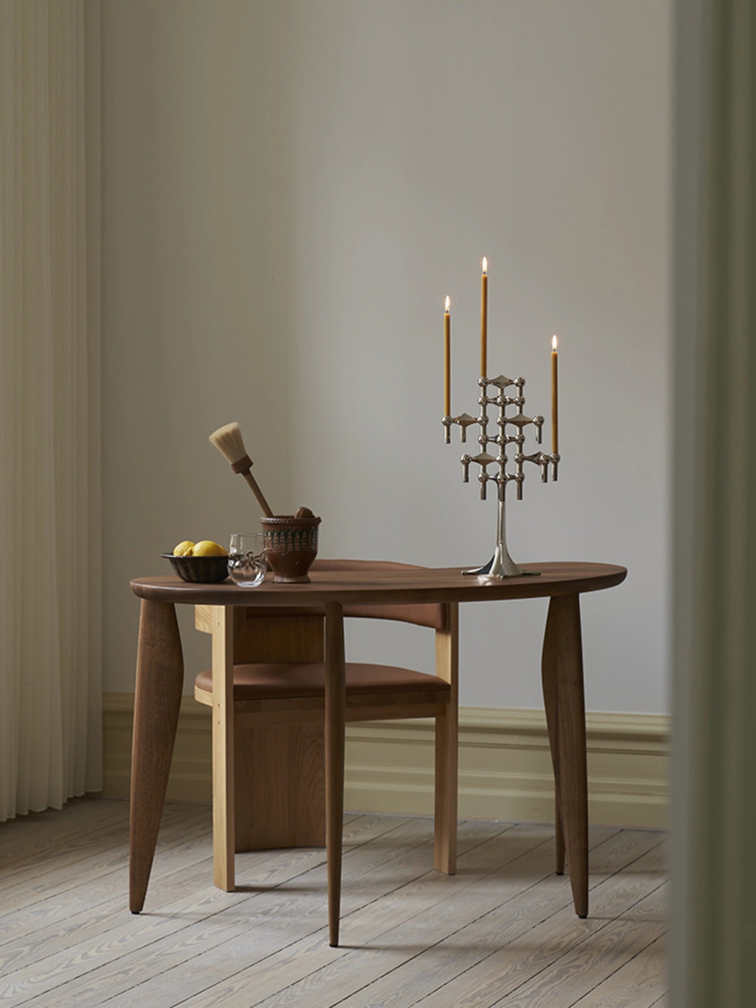 Stoff nagel candles in the iconic stoff nagel candle holders on top of a wooden designer dining table. Elegant dining setting.