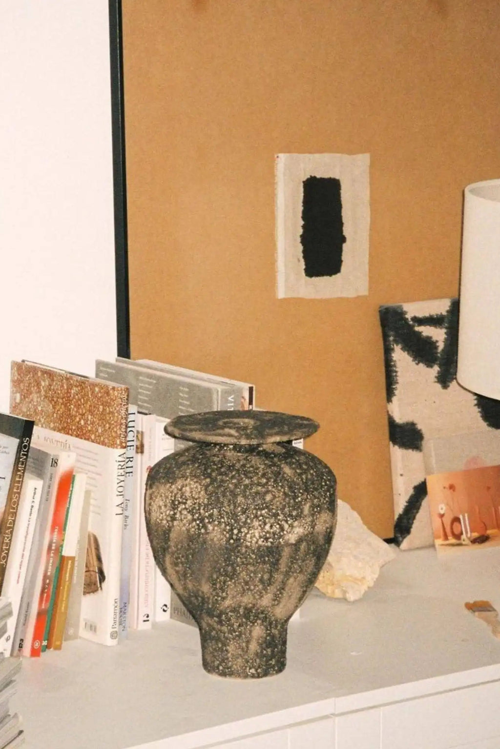 Canoa Lab Isolated n.7 Vase, a handcrafted dark mottled ceramic vase featuring a deeply textured, porous volcanic finish in tones of charcoal and bronze, with an organic urn-like silhouette and a flat, removable lid. This brutalist stoneware vase is an ideal statement piece for organic modern shelf styling or wabi-sabi living room decor.