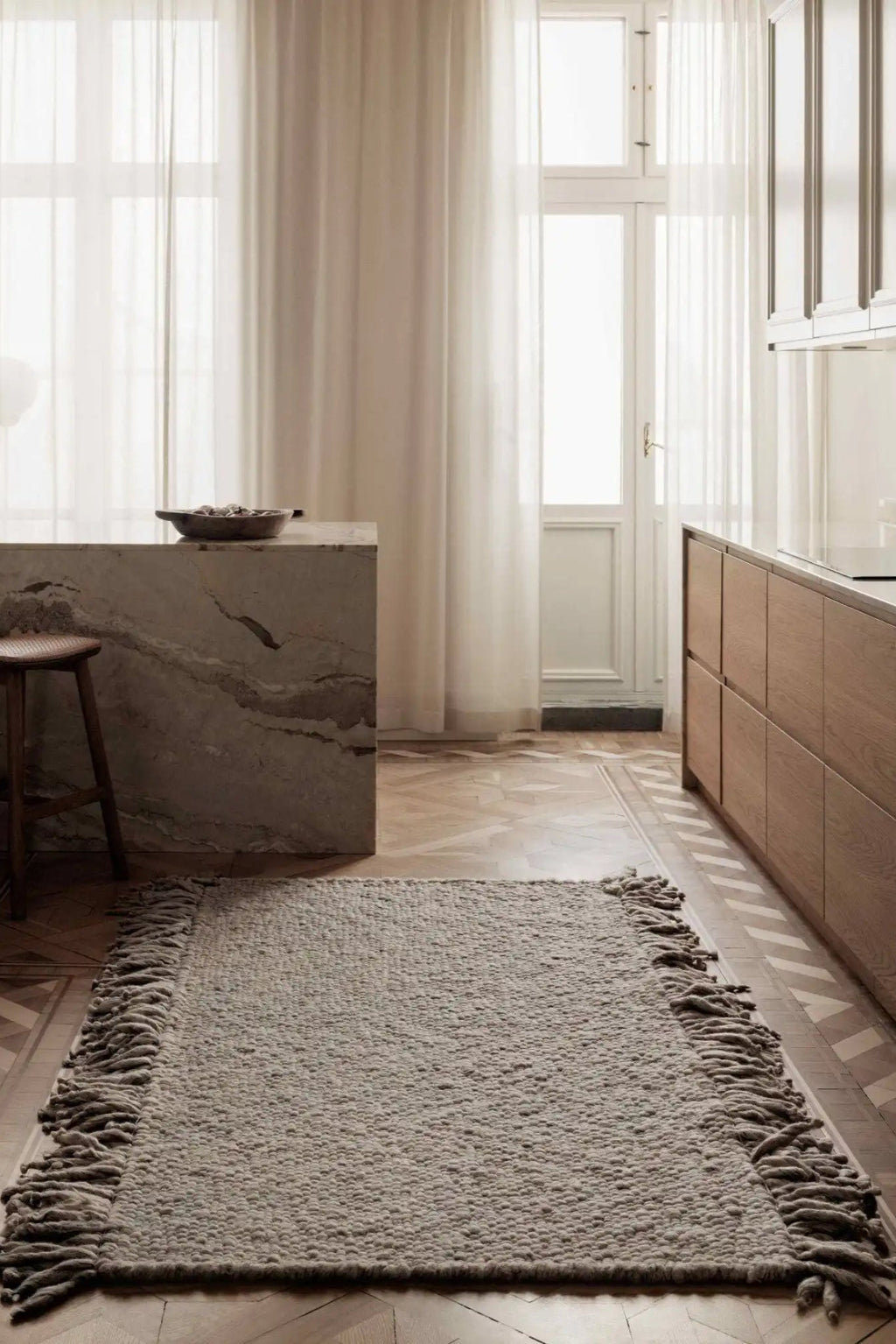 Cappelen Dimyr Colonnade No.03 Rug, a hand-knotted wool area rug in a natural grey-taupe shade, featuring a plush, textured shaggy pile and distinctive long fringe along the shorter edges. This organic modern rug adds warmth and tactile appeal, perfect for Scandinavian living rooms, cozy bedrooms, or a minimalist kitchen accent.