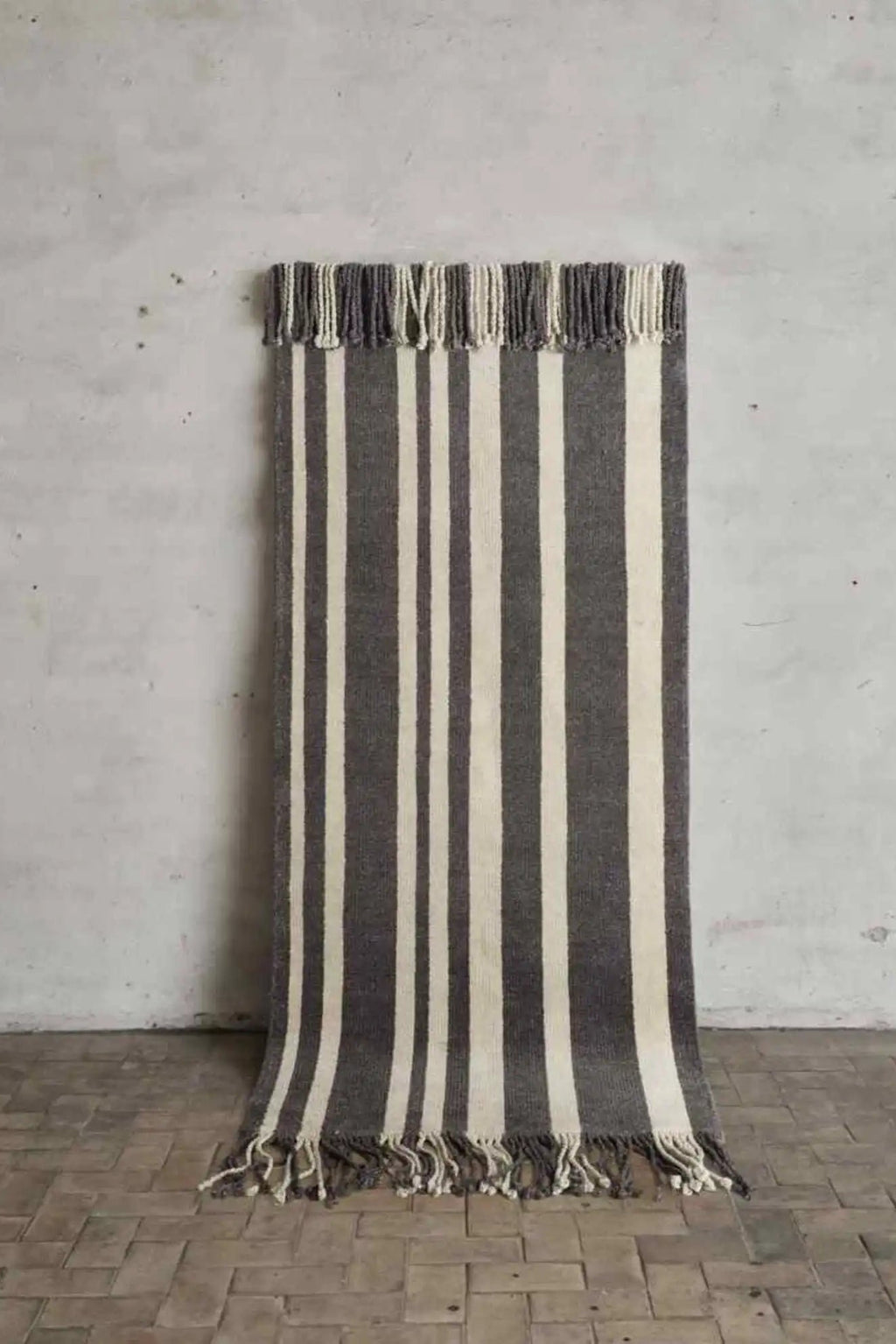 Cappelen Dimyr Colonnade No.05 Rug, a hand-woven wool runner rug featuring bold vertical stripes in dark grey and off-white with textured fringes on both ends. This minimalist Scandinavian design offers an organic modern feel with its natural fiber construction and artisanal texture. Ideal as a stylish hallway runner or a cozy accent rug for bedrooms and living rooms.