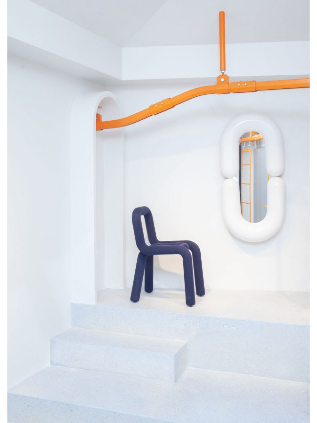 Moustache Bold Chair, a dark blue fabric-upholstered contemporary chair featuring a continuous tubular frame with soft, padded contours, creating a striking minimalist yet playful sculptural silhouette.