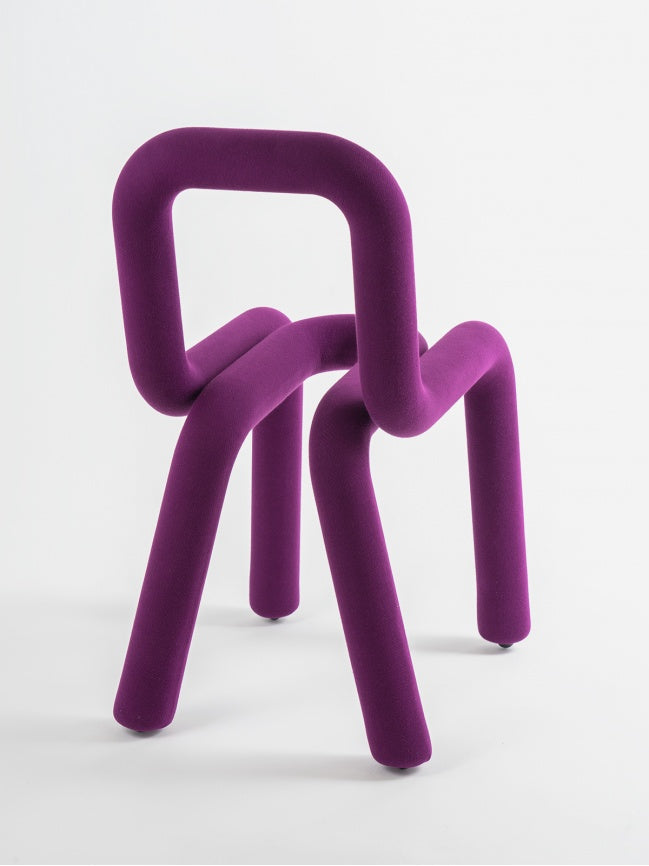 Moustache Bold Chair, a striking contemporary sculptural chair featuring a continuous tubular form entirely upholstered in a plush, deep purple velvet fabric. Its playful, exaggerated curves create a bold, art-inspired silhouette that redefines modern seating. Perfect as a statement accent chair for vibrant living rooms, postmodern dining spaces, or creative home offices.