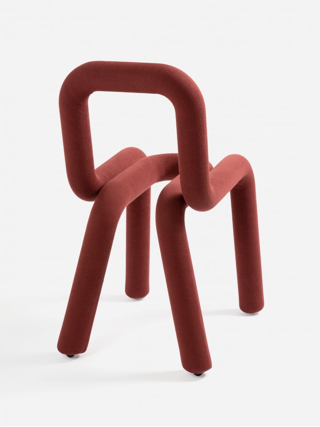 Moustache Bold Chair, a striking contemporary chair featuring a continuous tubular form fully upholstered in a rich terracotta red fabric. Its bold, sculptural silhouette creates a seamless backrest and legs from a single looped textile-covered metal tube, offering a soft yet impactful visual statement. Ideal as a modern accent chair or designer dining chair for minimalist or avant-garde interiors.