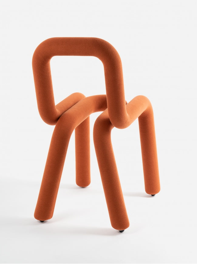 Moustache Bold Chair, a striking contemporary chair featuring a continuous tubular form, fully upholstered in a textured burnt orange fabric. Its bold, playful design creates a sculptural silhouette, forming the legs, seat, and backrest from a single fluid line. This iconic piece of art furniture is perfect as an accent chair for modern living rooms, creative studios, or unique dining spaces.