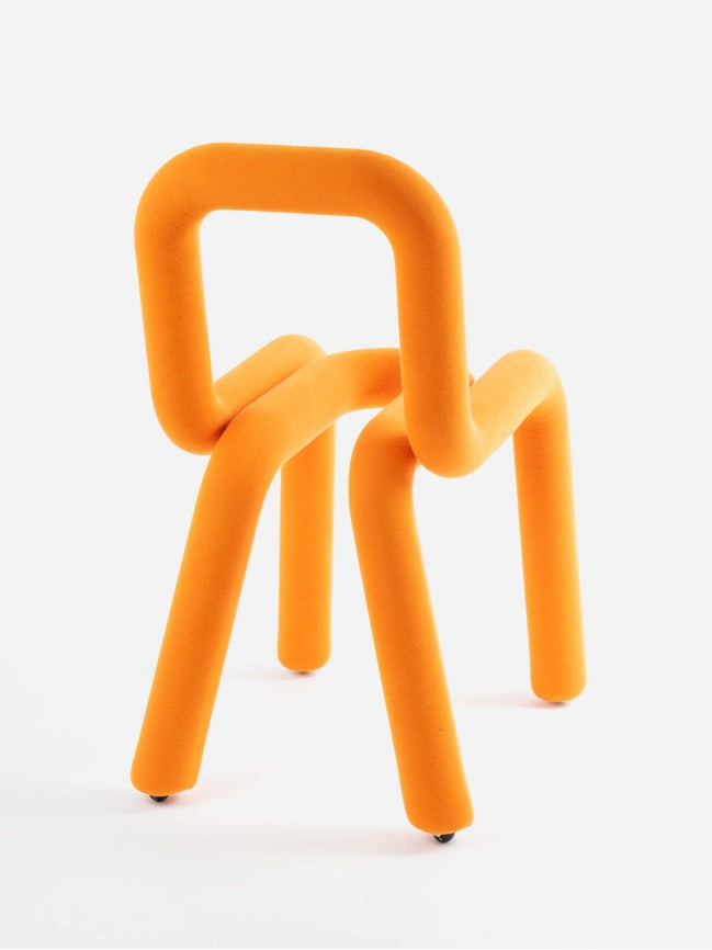 Moustache Bold Chair, a vibrant orange contemporary chair featuring a continuous tubular metal structure padded with soft polyurethane foam and upholstered in a fuzzy, velvet-like textile. Its playful, sculptural form creates a minimalist yet bold statement, with a seamless, curvilinear design functioning as both seat and backrest. Ideal as an eye-catching accent chair for a modern living room, creative office space, or eclectic dining area.
