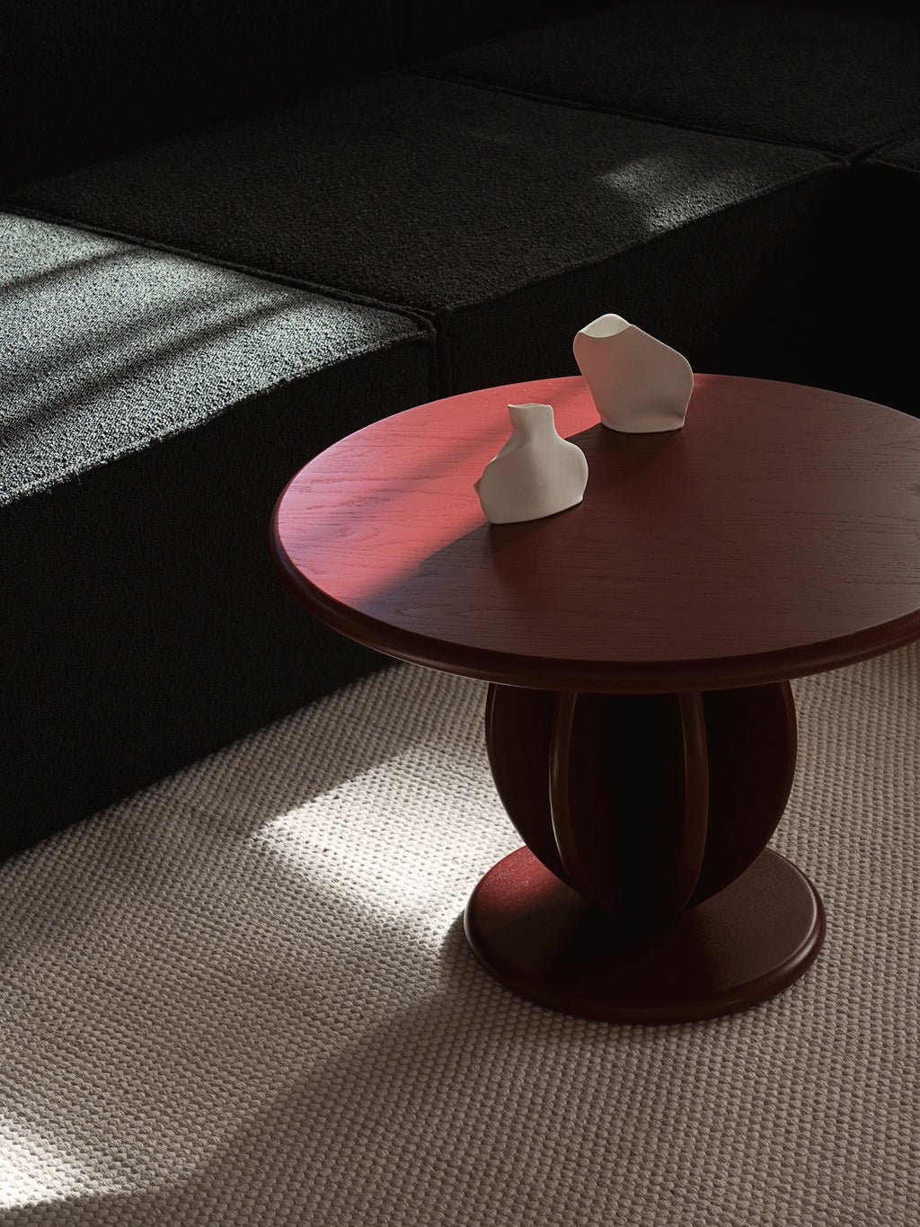 TAMO Citrus Coffee Table: A round, rich reddish-brown wood table with a unique curved, multi-petal base, styled with white ceramic vases on a textured rug. This premium, handcrafted piece offers distinctive modern home decor.