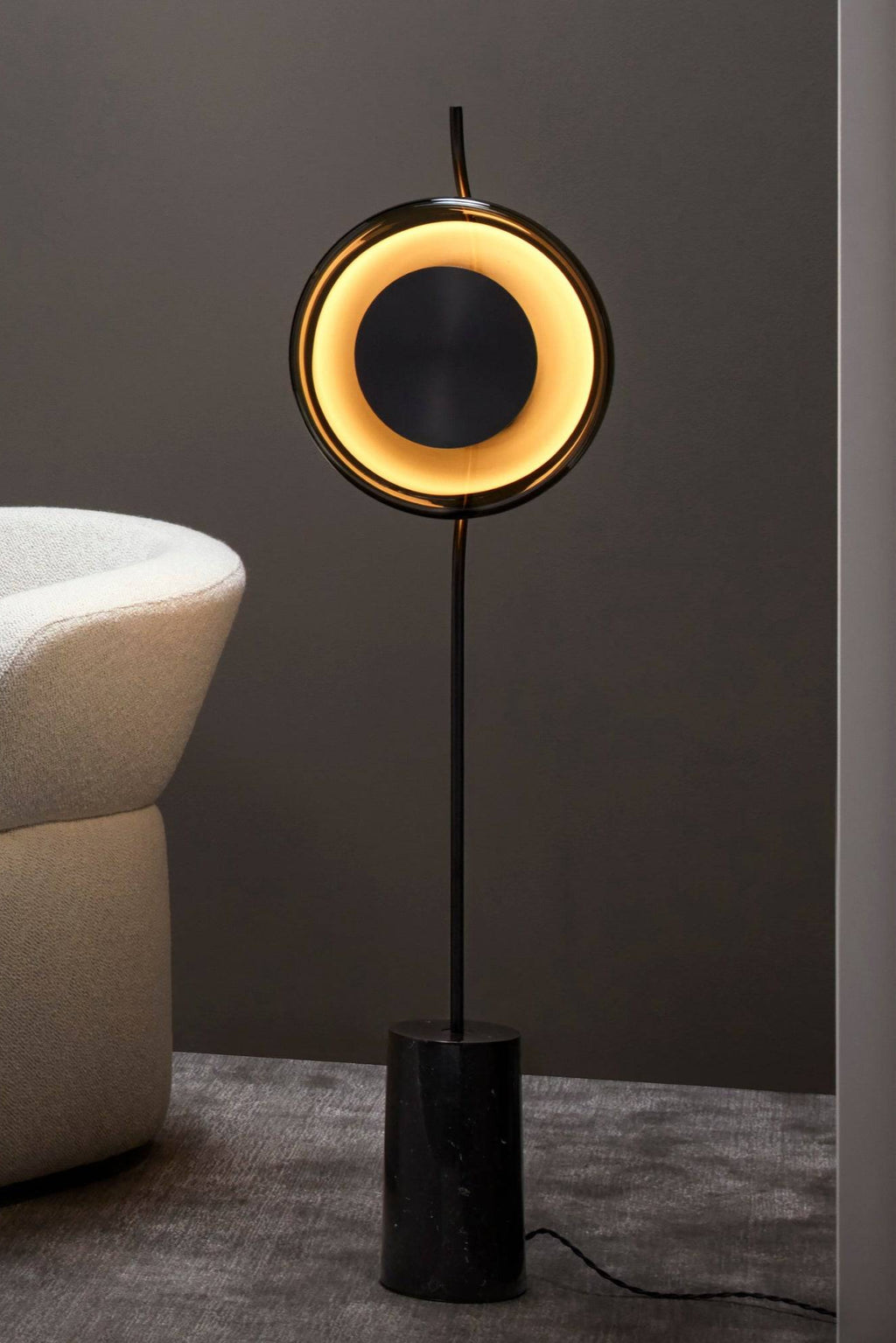 CTO Lighting Pendulum Floor Lamp, a contemporary luxury floor lamp featuring a polished black marble cylindrical base, a slender matte black metal stem, and a distinctive circular light head with a warm gold-toned glow surrounding a central black disc. This modern minimalist floor lamp is perfect for living room accent lighting or as a statement piece in sophisticated bedroom interiors.