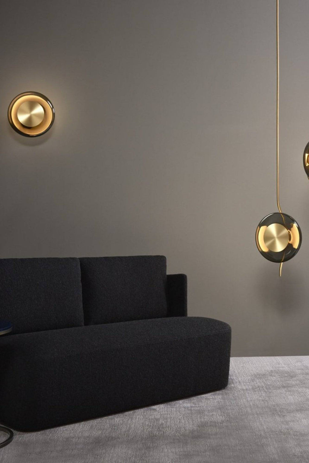 CTO Lighting Pendulum Wall Lamp, a luxurious modern wall light featuring a central brushed brass disc surrounded by a sleek smoked glass ring, emitting a warm ambient glow. This contemporary circular wall lamp offers sophisticated illumination, perfect for adding an Art Deco inspired accent to luxury living rooms, elegant bedrooms, or stylish entryways.