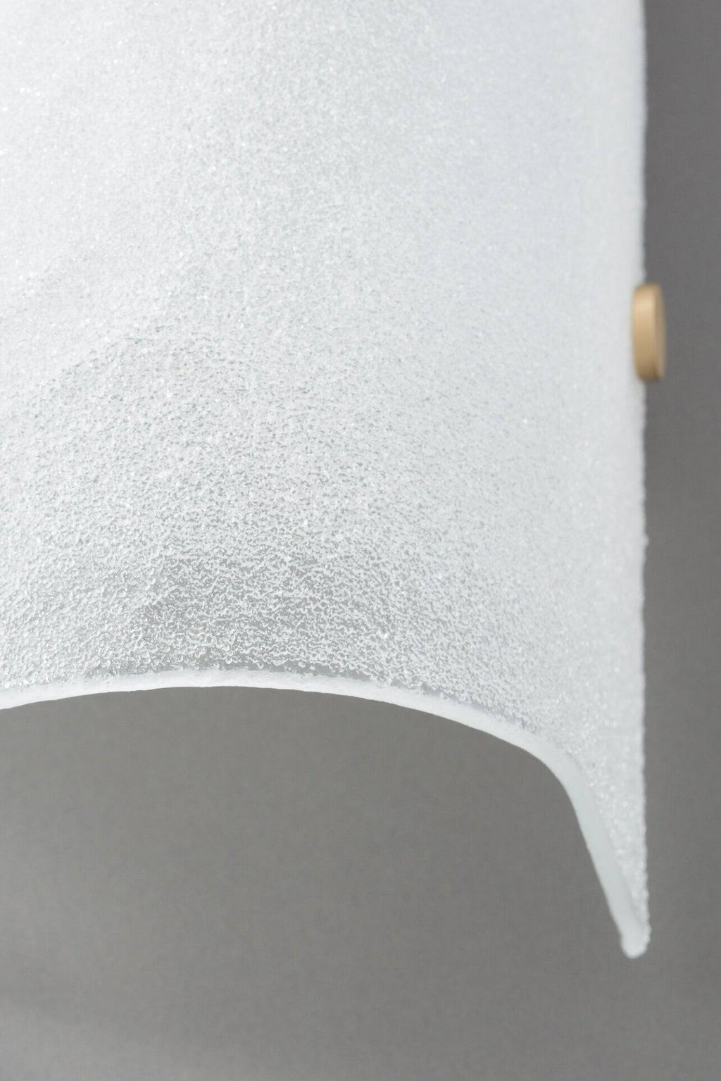 CTO Lighting Whistler Wall Lamp, a contemporary wall sconce crafted from heavily textured frosted glass with a granular, ice-like finish and a gently curved shape, accented by a subtle brass fixture. This luxurious modern lighting piece provides soft, diffused illumination, perfect for elegant living rooms, sophisticated bedrooms, or refined hallways.