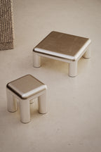 Two metallic and aluminium Formarkivet side table and coffee table on a plain concrete surface