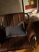 Gray pillow with scalloped edge on a brown leather chair