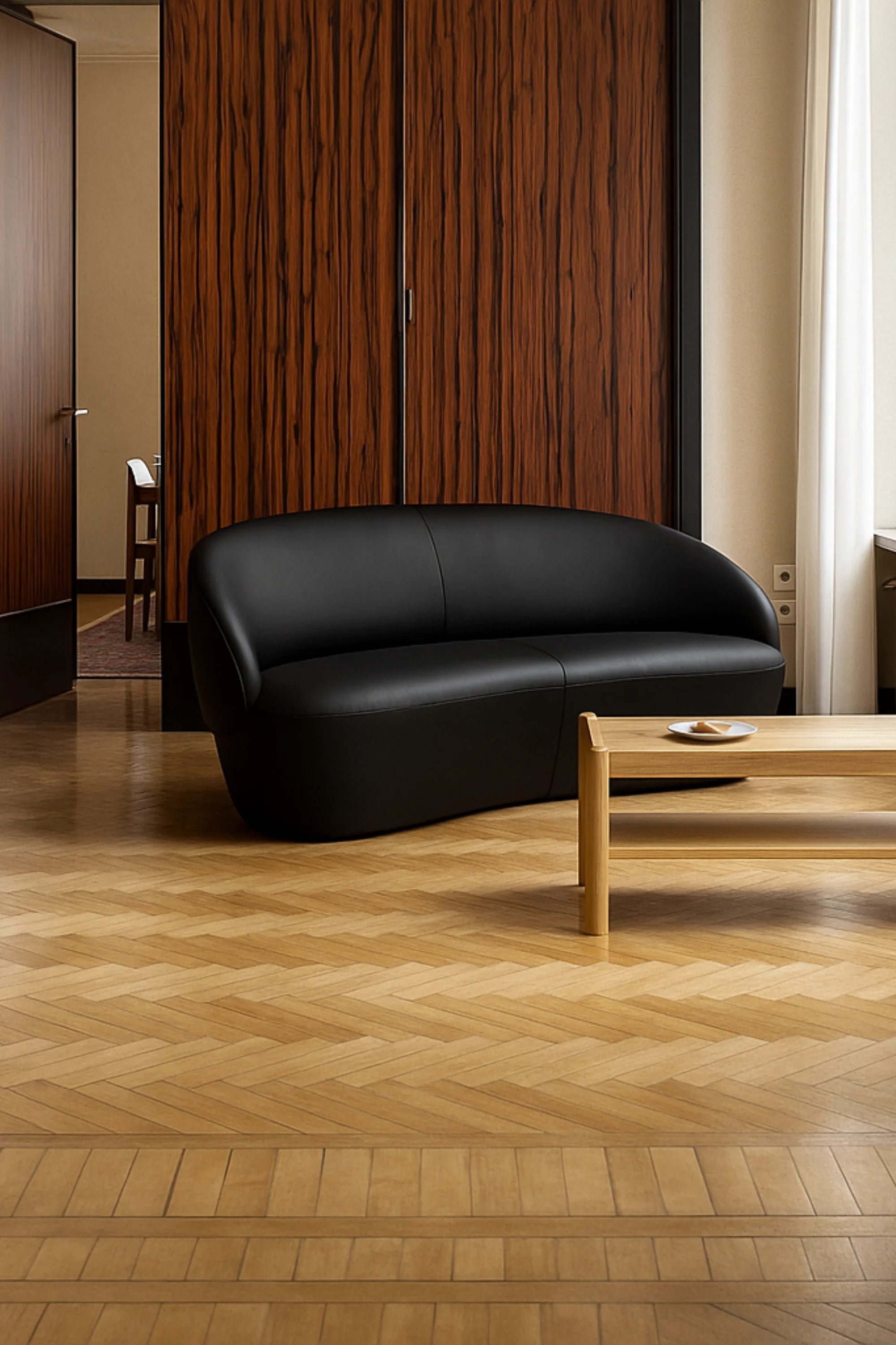 Black Naive 2-seater leather sofa in a room with wooden flooring and a wooden separator wall.