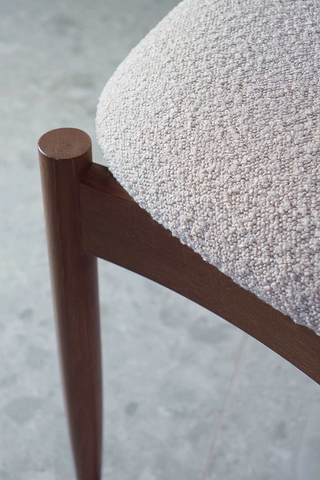 TAMO Kemi Chair, a refined contemporary dining chair showcasing a warm dark solid wood frame with a smooth, rounded leg and a deeply textured light cream bouclé upholstered seat.