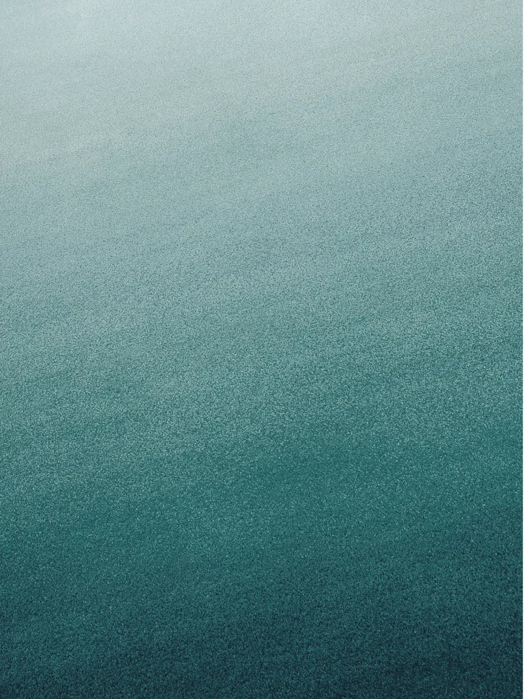 alp_ Degradé Double Rug, a contemporary gradient area rug featuring a smooth degradé ombre transition from light aqua blue to deep teal. It has a soft, plush textured pile, evoking a sense of depth and tranquility. This modern minimalist rug is perfect for adding a serene touch to a contemporary living room, a tranquil bedroom, or a stylish home office, creating a calming focal point.