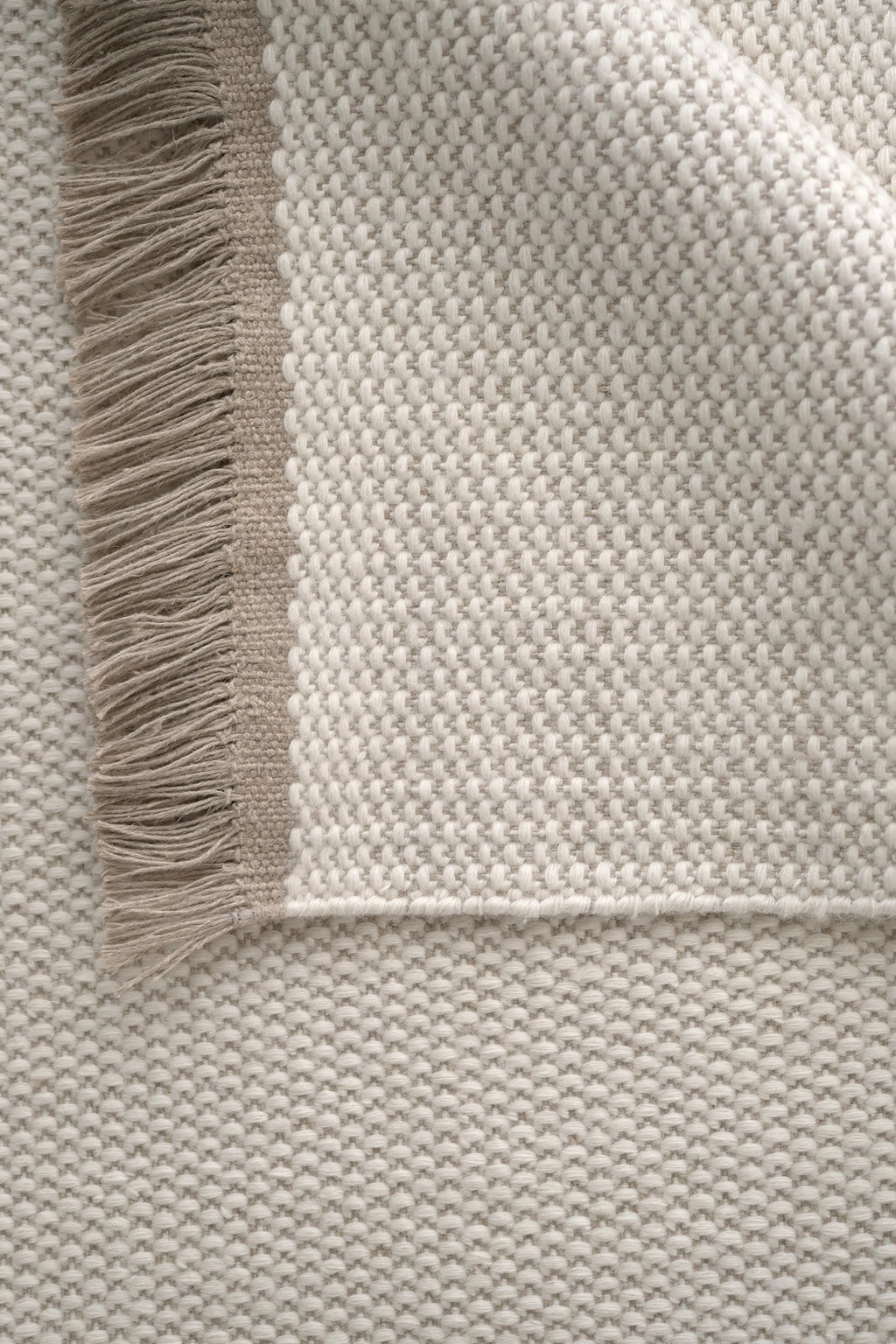 Linie Design Pastoral Unity Wool Rug, a hand-knotted wool area rug featuring a distinct two-tone textured pebble weave in natural undyed cream and light beige, creating a plush, tactile surface. It's accented with a soft, shaggy fringe in matching light beige, adding an organic touch. This Scandinavian-inspired minimalist rug is perfect for adding warmth and sophisticated texture to modern living rooms, bedrooms, or cozy reading nooks.