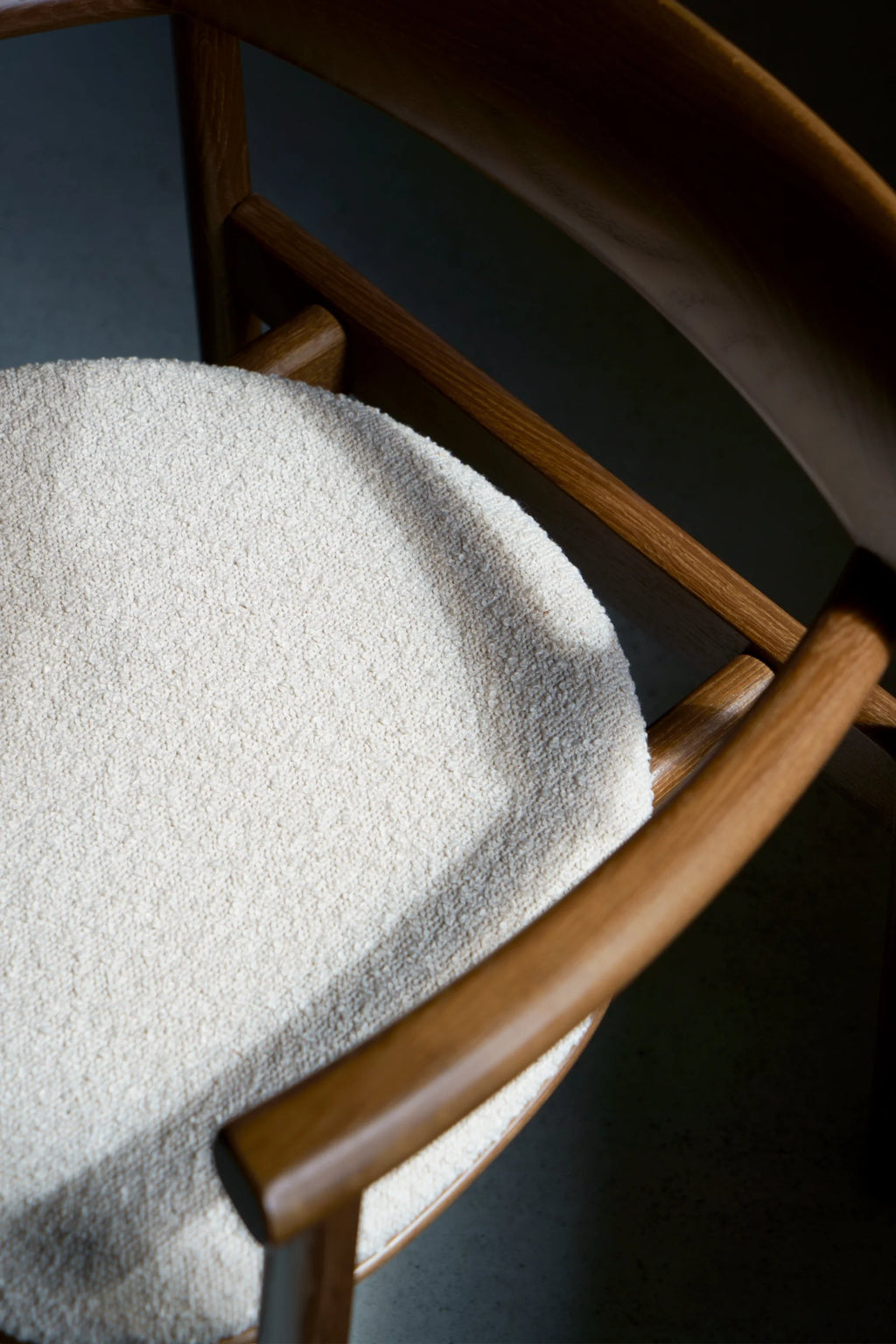 TAMO Elipsa Chair: Close-up top view of the premium cream bouclé upholstered seat with visible texture, framed by polished light brown wooden armrests and back support. Ideal for modern living spaces.