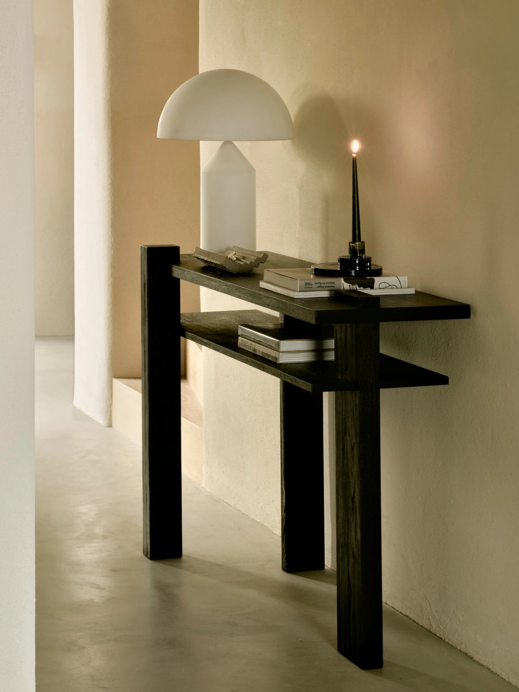 Ethnicraft Abstract Console in Teak Black, styled in a contemporary living space, featuring its dark wood finish, adorned with a white mushroom lamp, books, and a candle, against a warm, neutral wall.