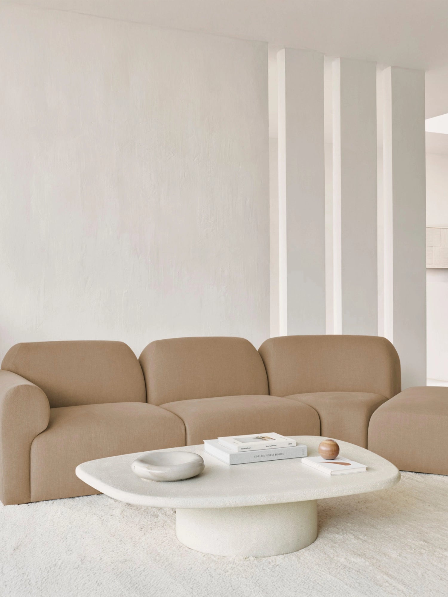 Ethnicraft Bulky Modular Sofa in a light beige, soft fabric, configured as a multi-seater unit in a bright, minimalist living space. The rounded, inviting design is paired with a unique, organic-shaped white coffee table, creating a serene atmosphere.