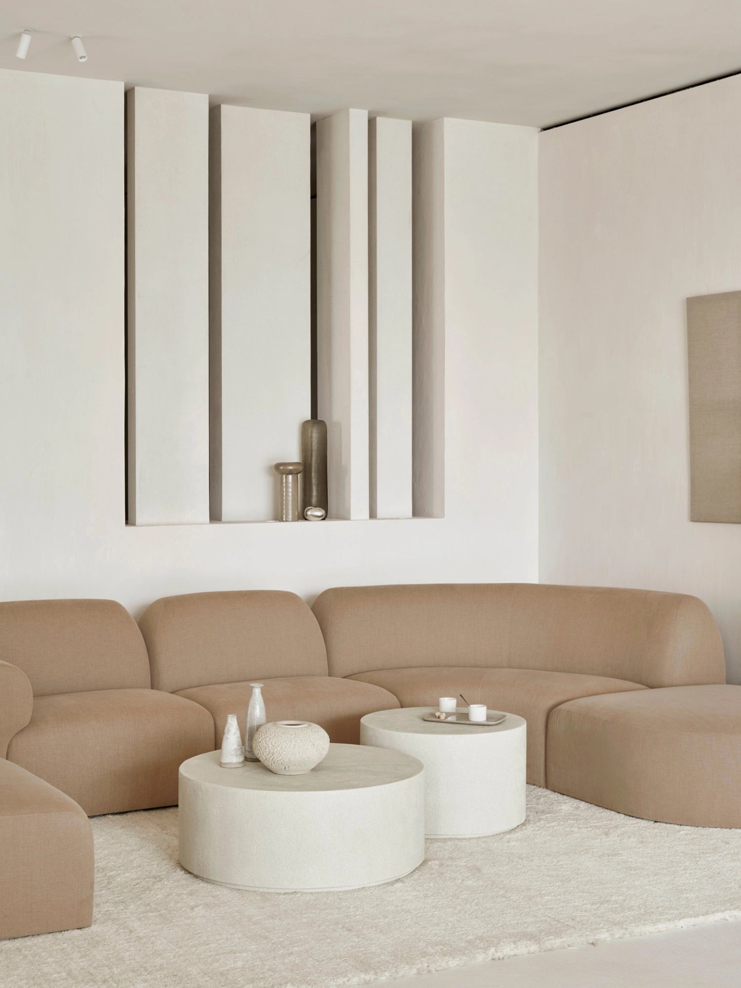 Ethnicraft Bulky Modular Sofa in a warm, light beige fabric, arranged as a large L-shaped sectional in a modern living room. The plush, rounded design exudes comfort and contemporary style, complemented by white coffee tables and minimalist decor.