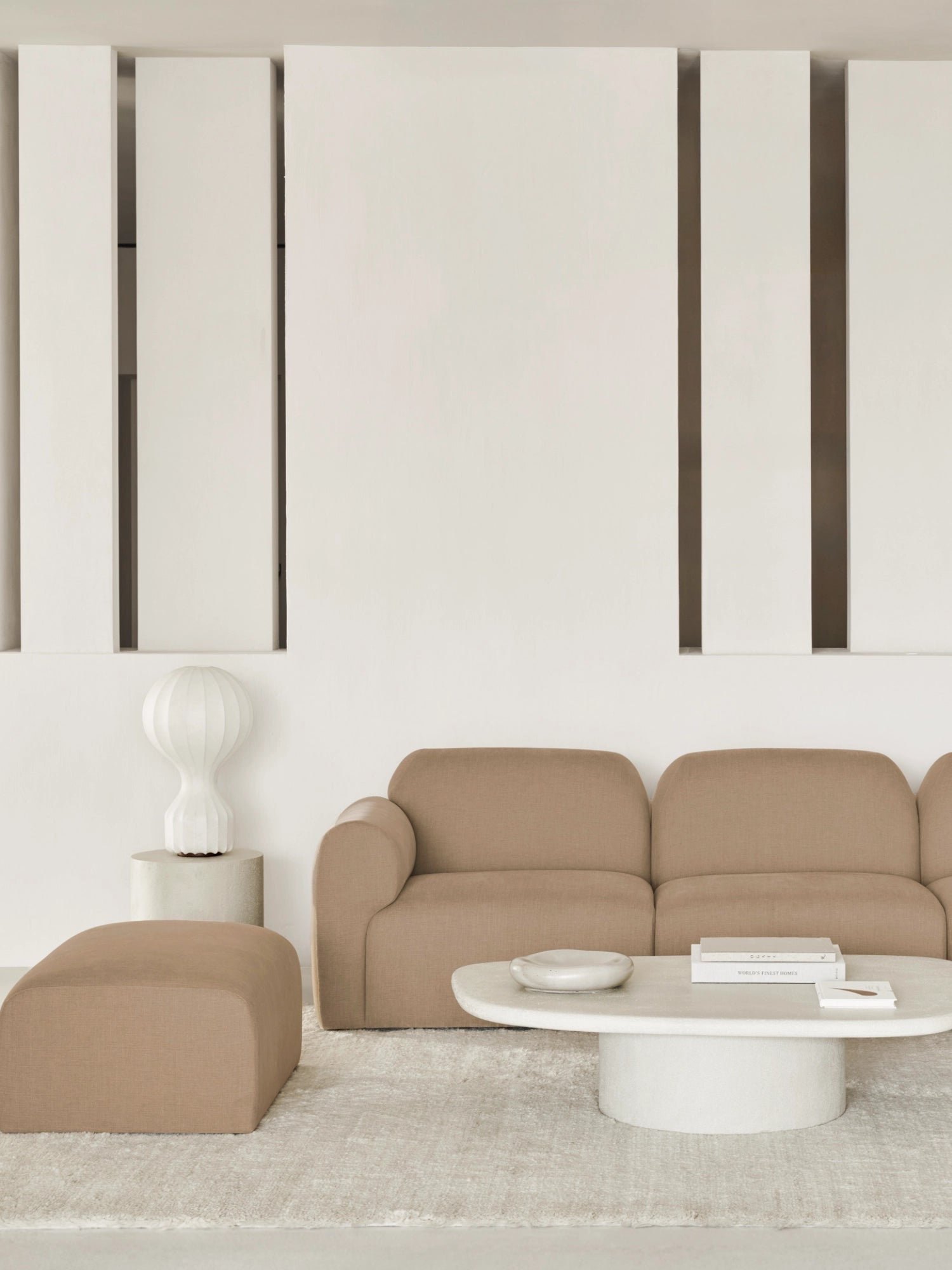 Ethnicraft Bulky Modular Sofa footstool module in a lifestyle setting. The beige fabric footstool complements a matching modular sofa, a white coffee table, and a textured rug, creating a modern, inviting living room ambiance with natural light.