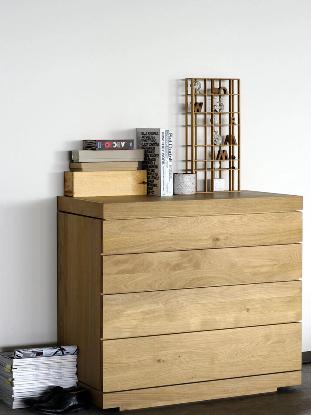 Ethnicraft Burger Dresser in natural oak, a modern wooden chest of drawers with four spacious, handle-less drawers, displayed in a stylish living room setting with books and decor on top.