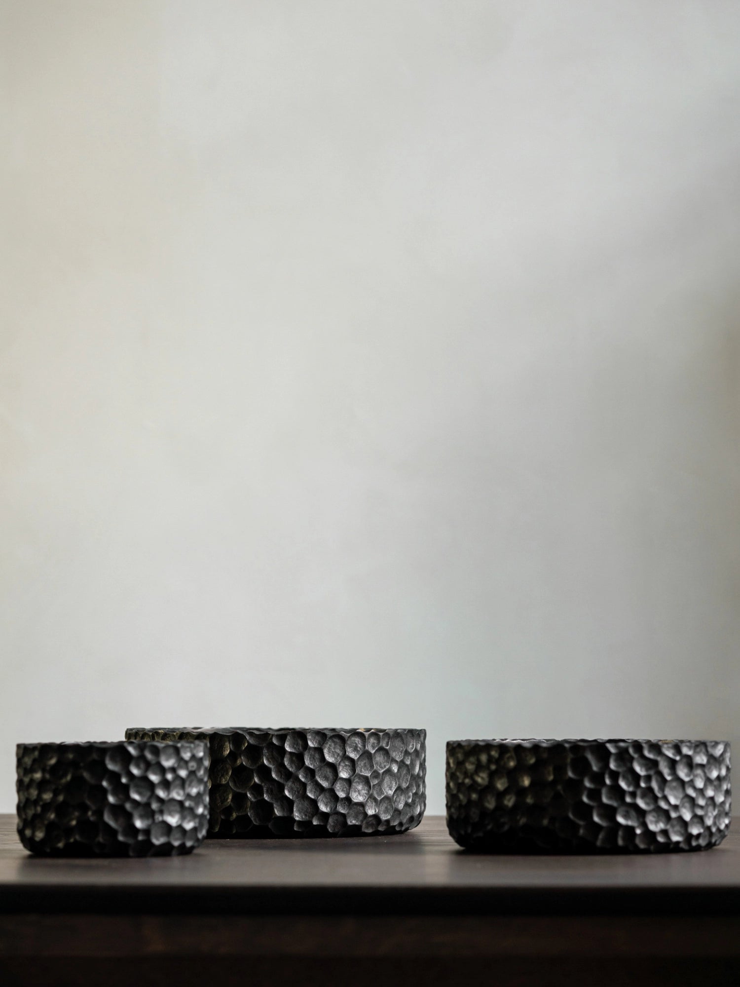 Ethnicraft Chopped Bowl Set, three dark brown wooden bowls with a unique, textured chopped surface, varying in size, elegantly displayed on a dark wooden surface against a light, minimalist wall.