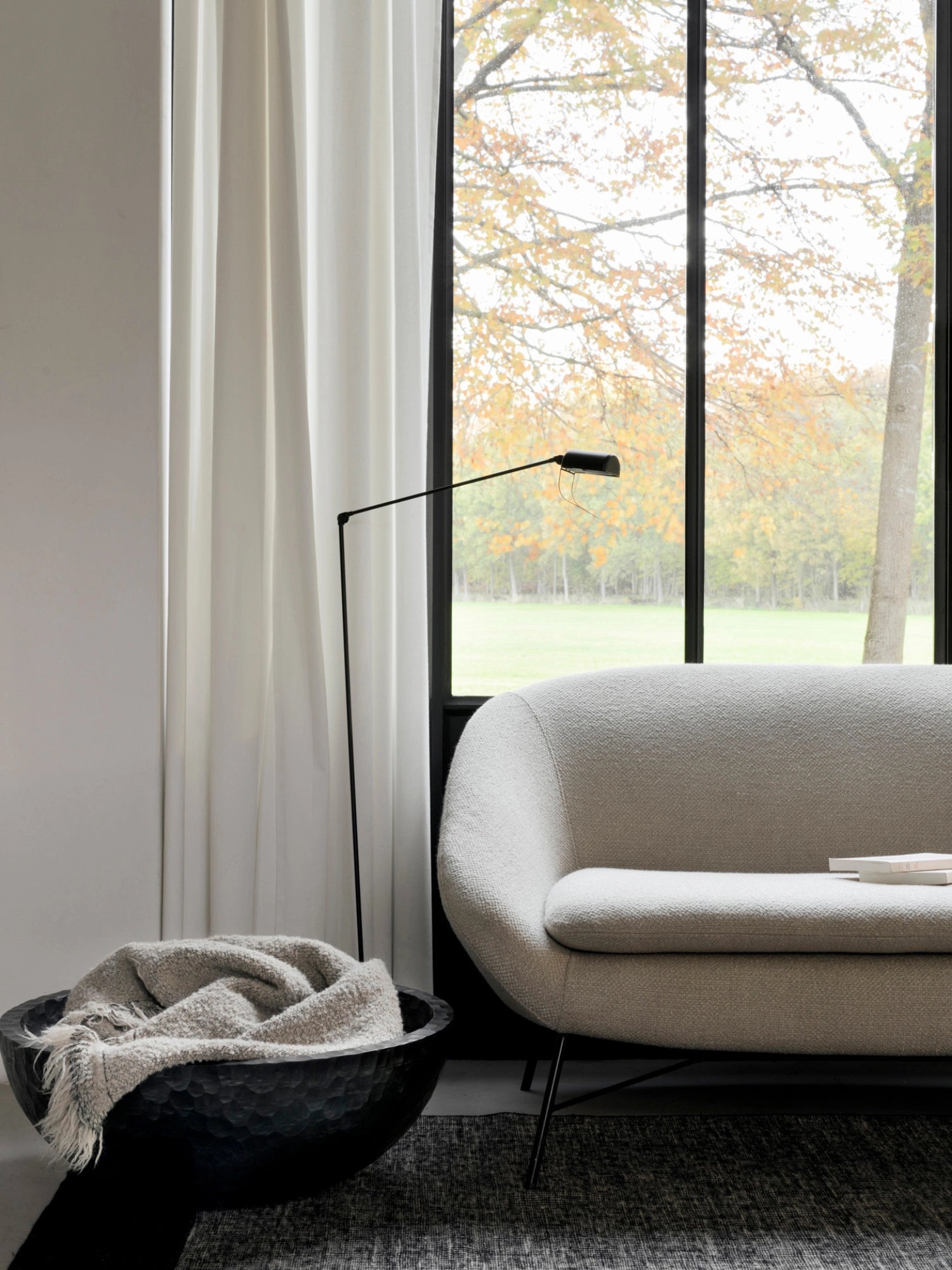 Ethnicraft Chopped XL Bowl, a large, dark, textured wooden bowl filled with a cozy light-colored throw blanket, positioned next to a modern cream sofa and a tall black lamp in a stylish living room setting.