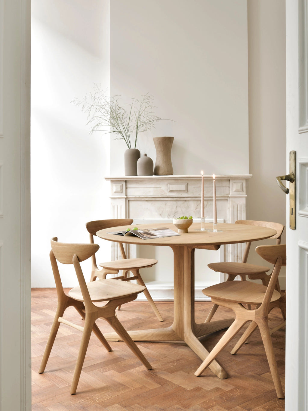 Ethnicraft Corto Dining Table, round oak, set in an elegant dining room with a classic fireplace, adorned with candles and vases, creating a warm, inviting atmosphere.