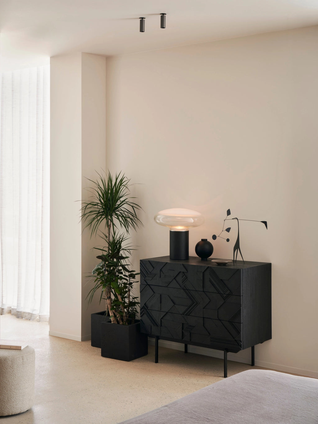 Ethnicraft Graphic Dresser in dark teak wood with a striking geometric pattern, styled in a modern bedroom setting. The elegant black dresser features sleek legs and is adorned with a contemporary lamp and plant, creating a sophisticated ambiance.