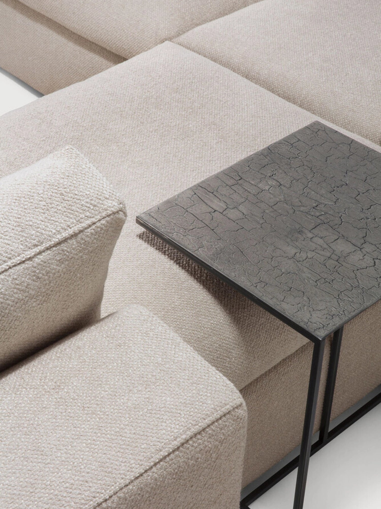 Ethnicraft Mellow Modular Sofa, showcasing the luxurious light beige textured fabric and plush cushions, with a modern dark side table featuring a cracked pattern.