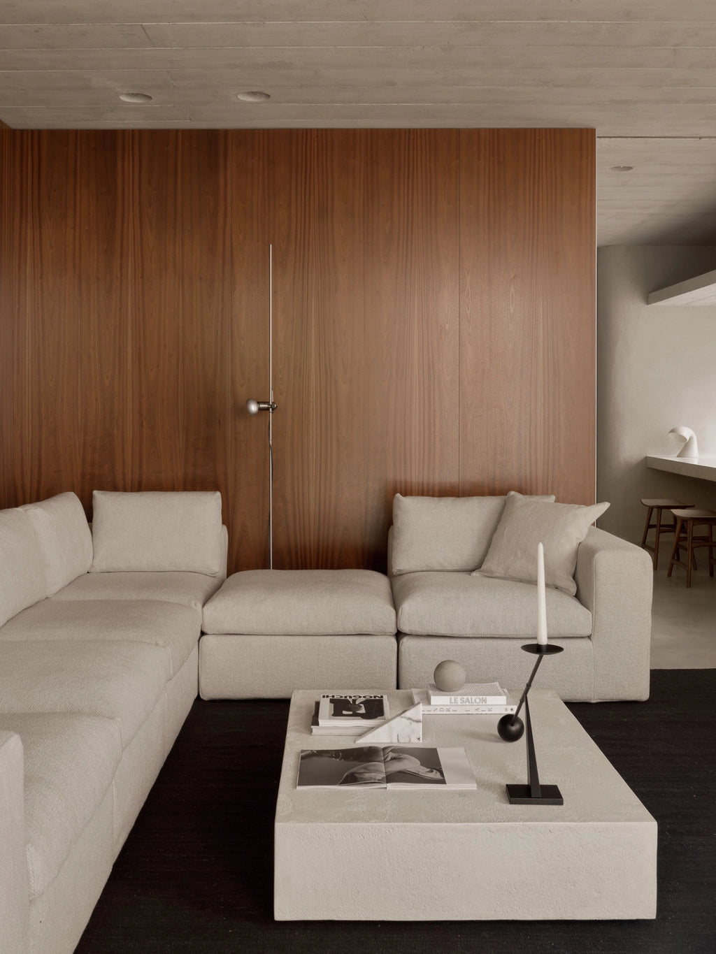Ethnicraft Mellow Modular Sofa in a light beige fabric, arranged in an L-shape with a matching footstool, paired with a modern concrete coffee table in a stylish living room.