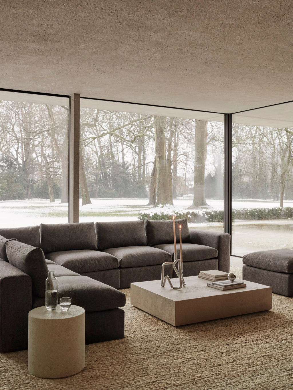 Ethnicraft Mellow Modular Sofa, 1-Seater. Expansive lifestyle shot of the dark grey modular sofa in a contemporary living room with large windows overlooking a snowy landscape, creating a cozy ambiance.