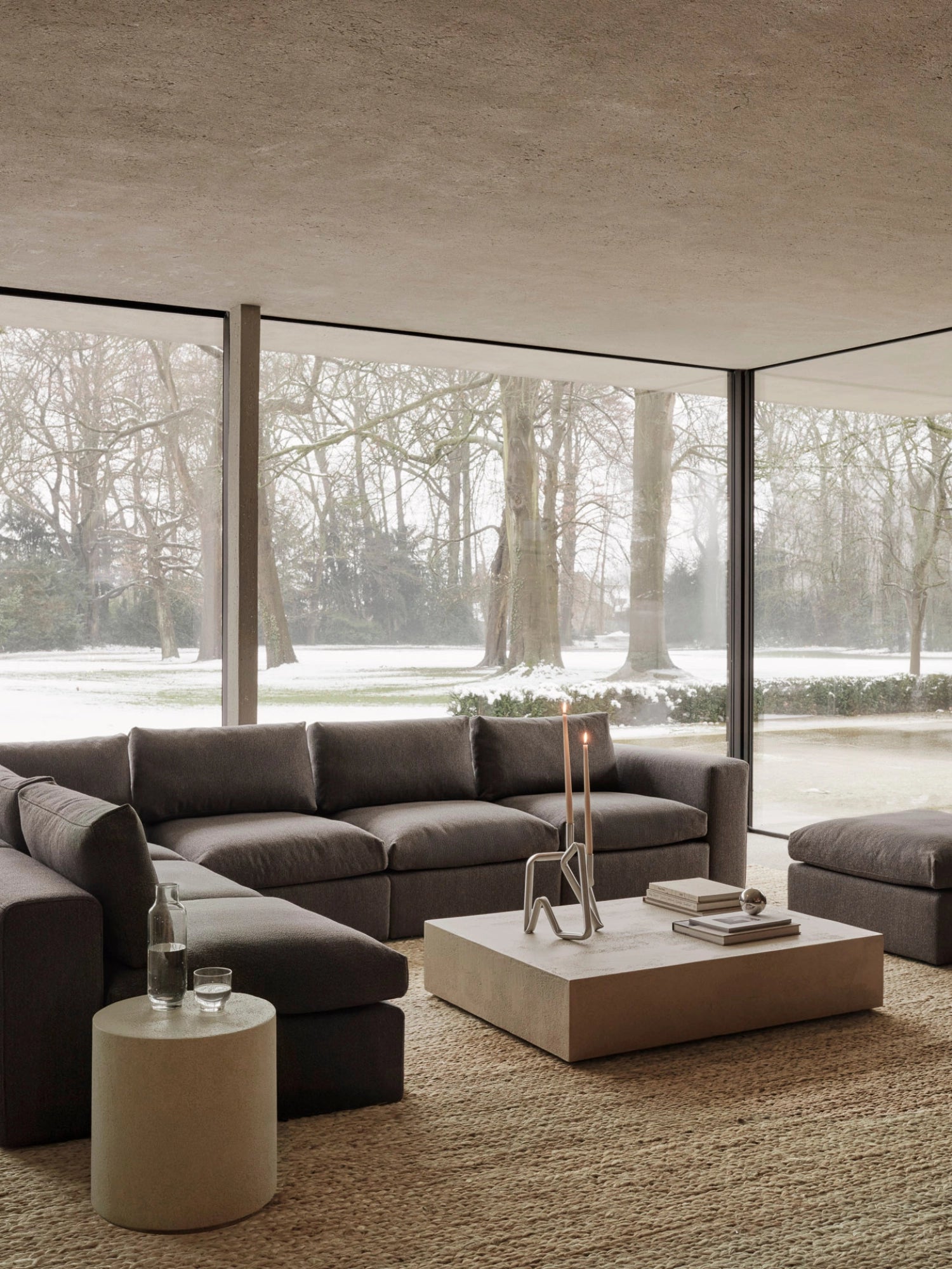 Ethnicraft Mellow Modular Sofa, 1-Seater. Expansive lifestyle shot of the dark grey modular sofa in a contemporary living room with large windows overlooking a snowy landscape, creating a cozy ambiance.