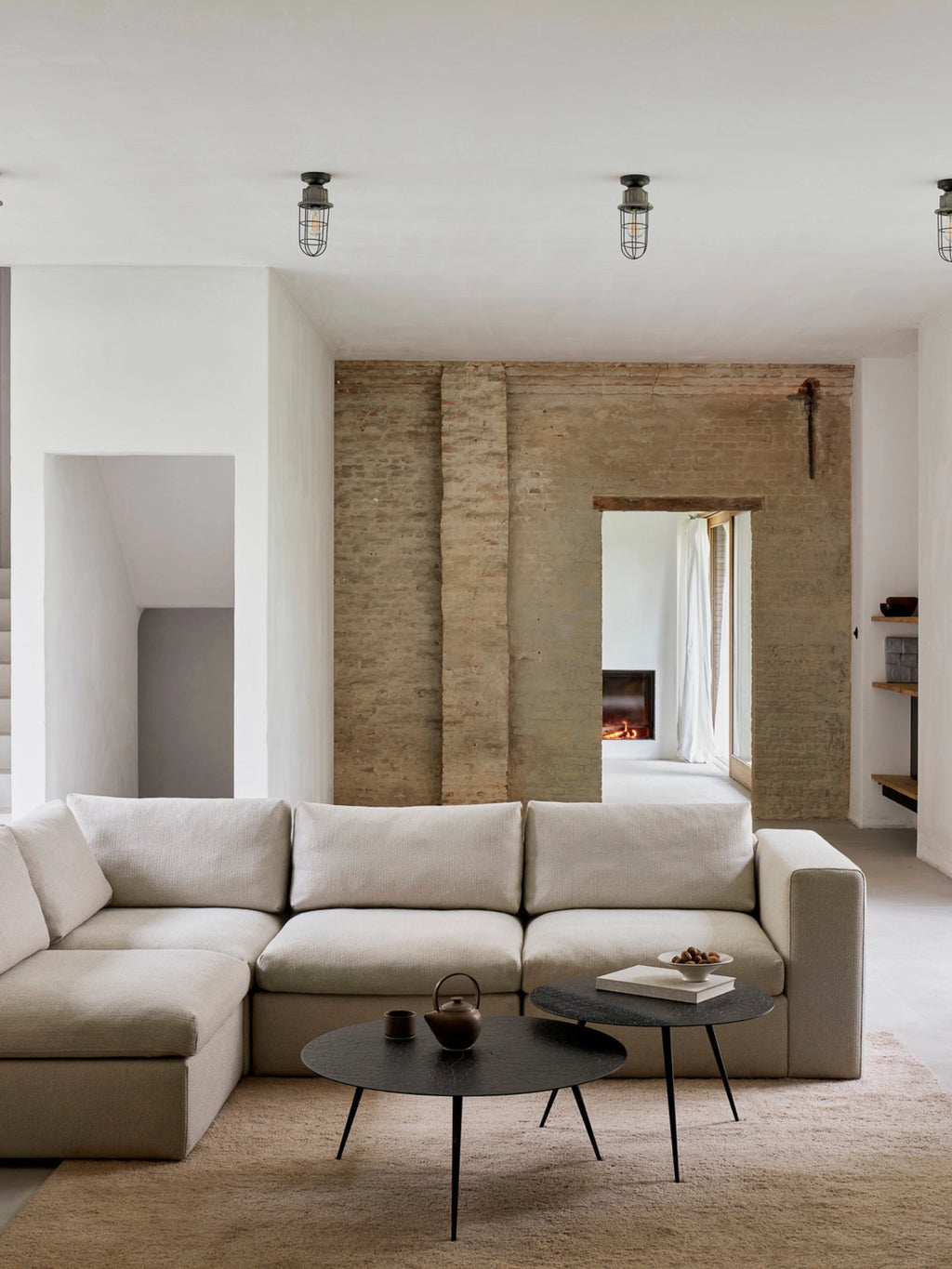 Ethnicraft Mellow Modular Sofa, a luxurious light beige L-shaped sectional, featuring soft, textured fabric, plush cushions, and a modern, low-profile design, elegantly arranged in a spacious living room with exposed brick walls and industrial lighting.
