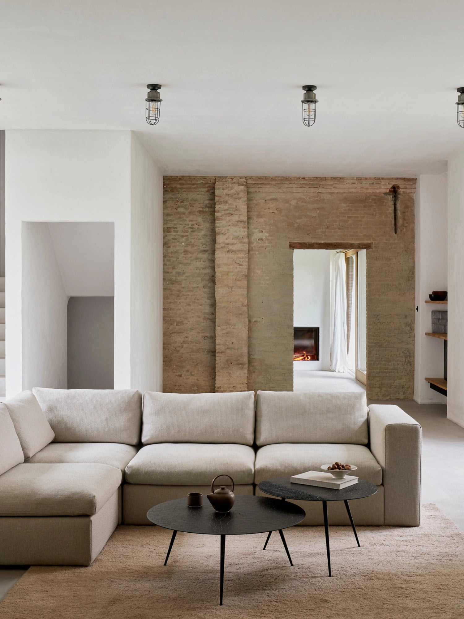 Ethnicraft Mellow Modular Sofa, a luxurious light beige L-shaped sectional, featuring soft, textured fabric, plush cushions, and a modern, low-profile design, elegantly arranged in a spacious living room with exposed brick walls and industrial lighting.