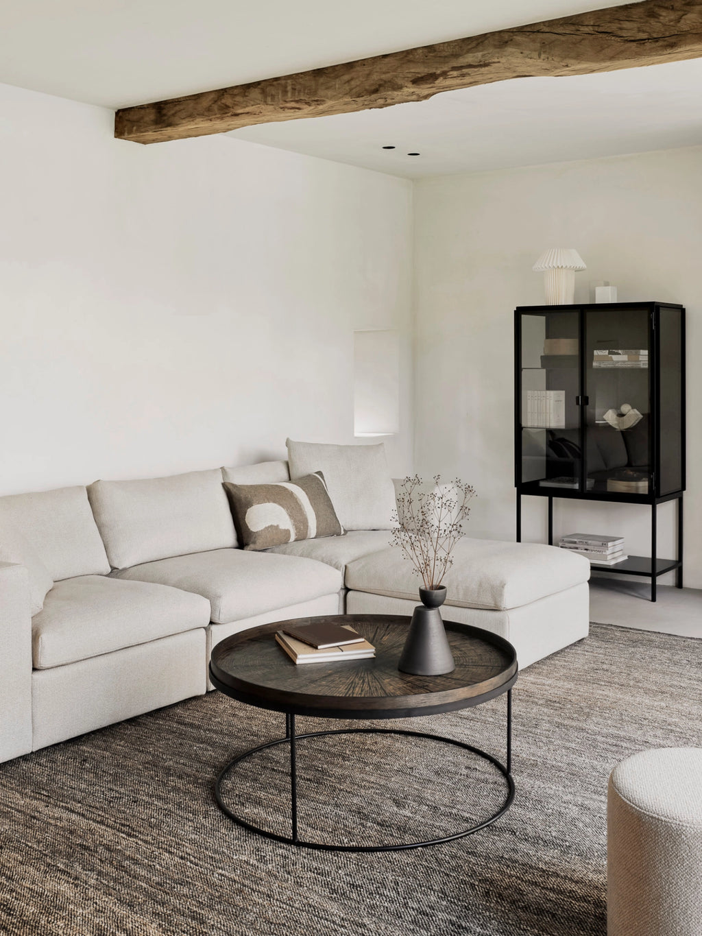 Ethnicraft Mellow Modular Sofa in a spacious, modern living room. This light beige sectional sofa with a chaise lounge is arranged around a dark wood coffee table, creating a cozy and inviting atmosphere.