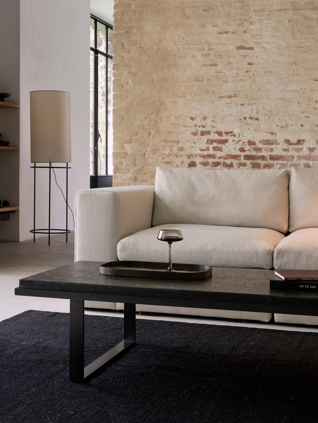 Ethnicraft Mellow Modular Sofa, a full sectional in a modern living room, featuring a cream-colored, textured fabric, paired with a dark coffee table and a brick accent wall, creating a cozy ambiance.