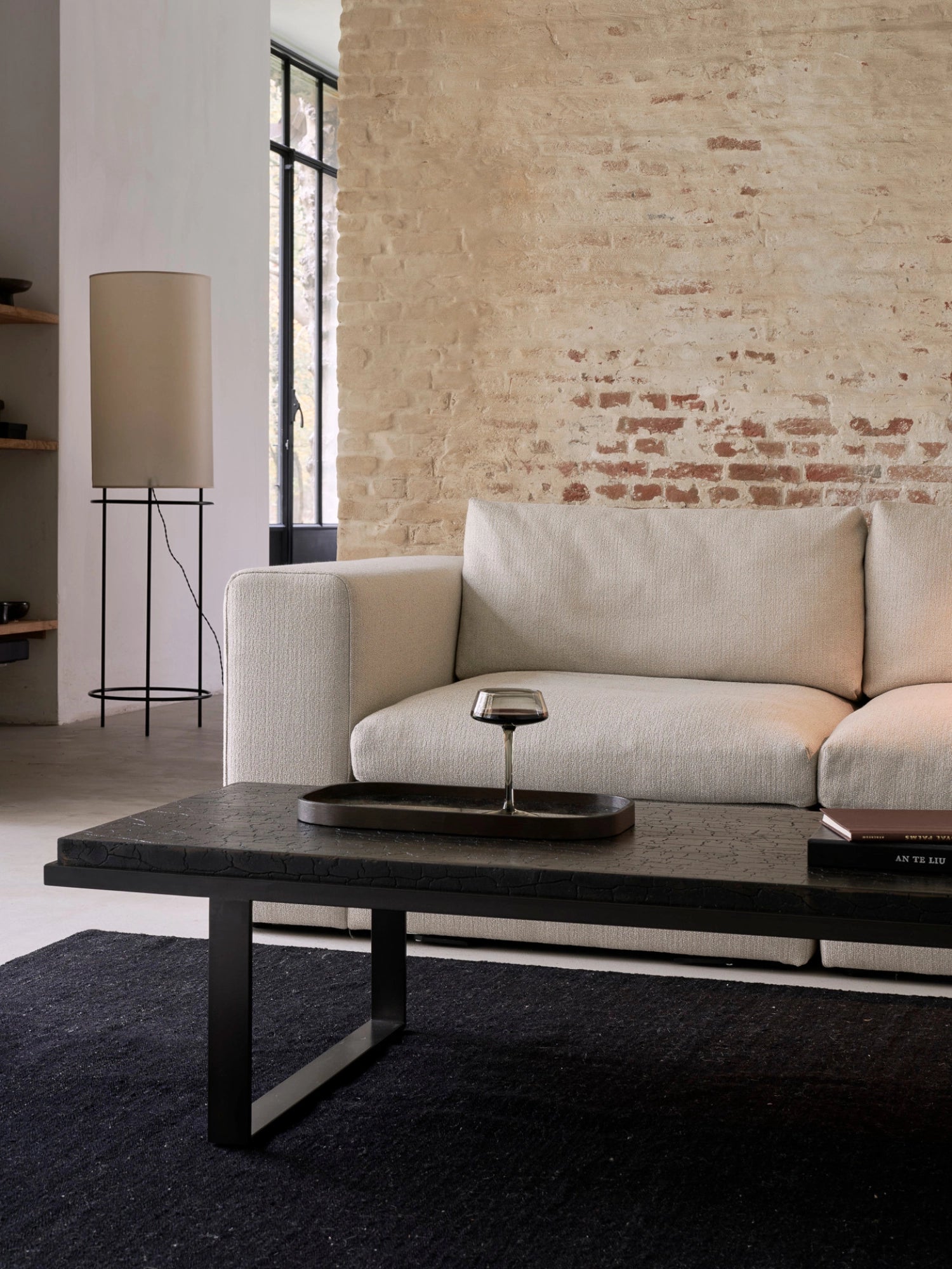 Ethnicraft Mellow Modular Sofa, a full sectional in a modern living room, featuring a cream-colored, textured fabric, paired with a dark coffee table and a brick accent wall, creating a cozy ambiance.