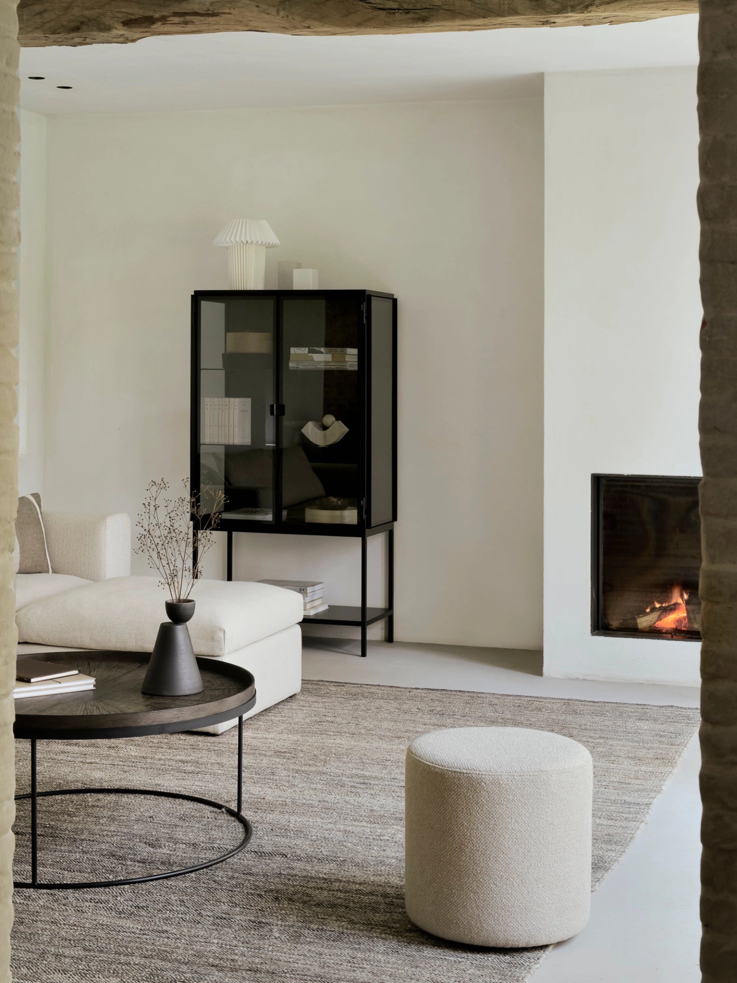 Ethnicraft Mellow Modular Sofa footstool in a stylish living room, complementing a cream sofa, with a dark round coffee table and a fireplace, creating a warm, inviting atmosphere.
