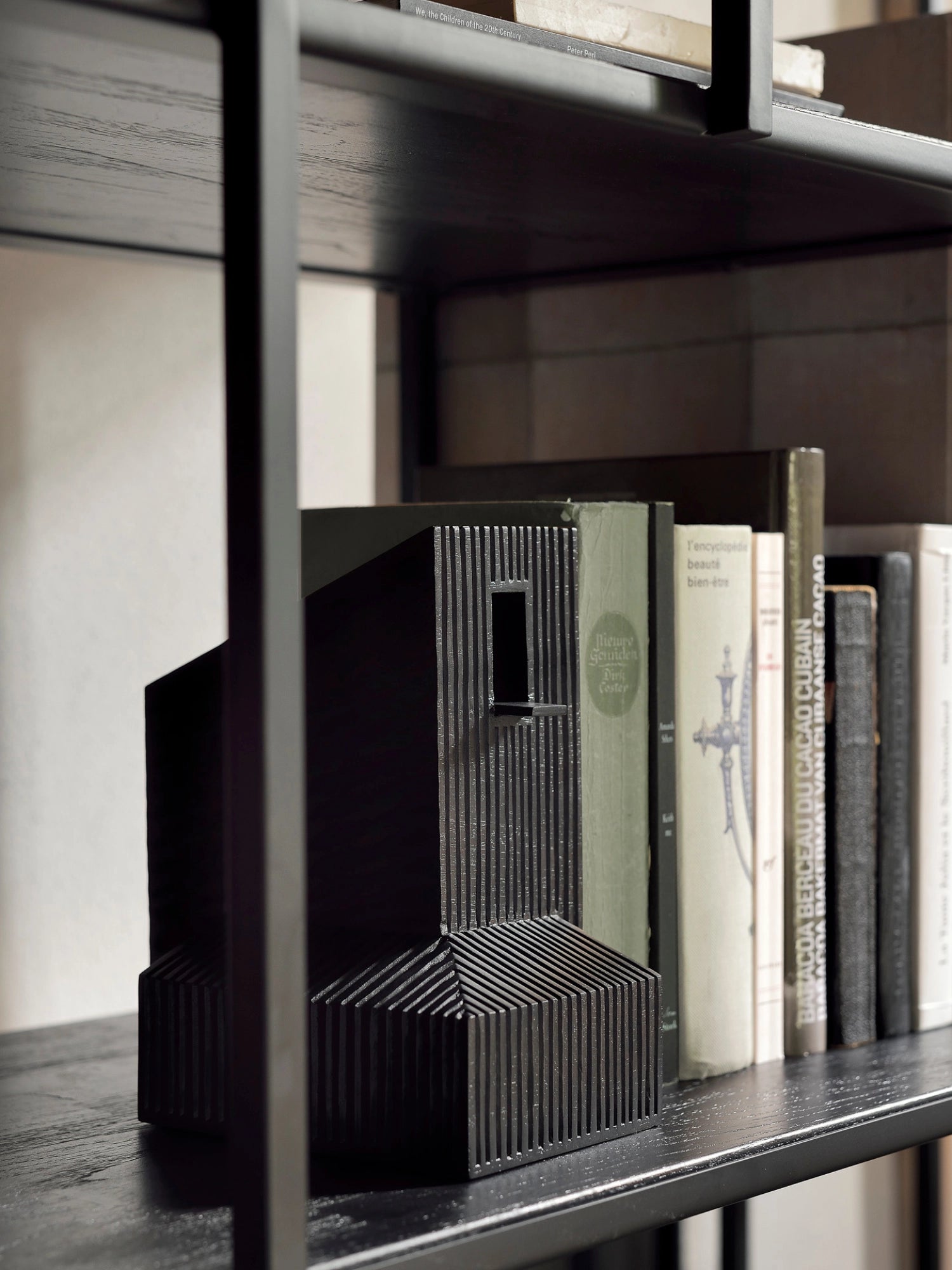 Ethnicraft Modern Farmhouse Object, a black wooden sculpture with ribbed details, resembling a modern building, placed on a dark wooden bookshelf alongside books. The dark wood grain and intricate design add a sophisticated touch.