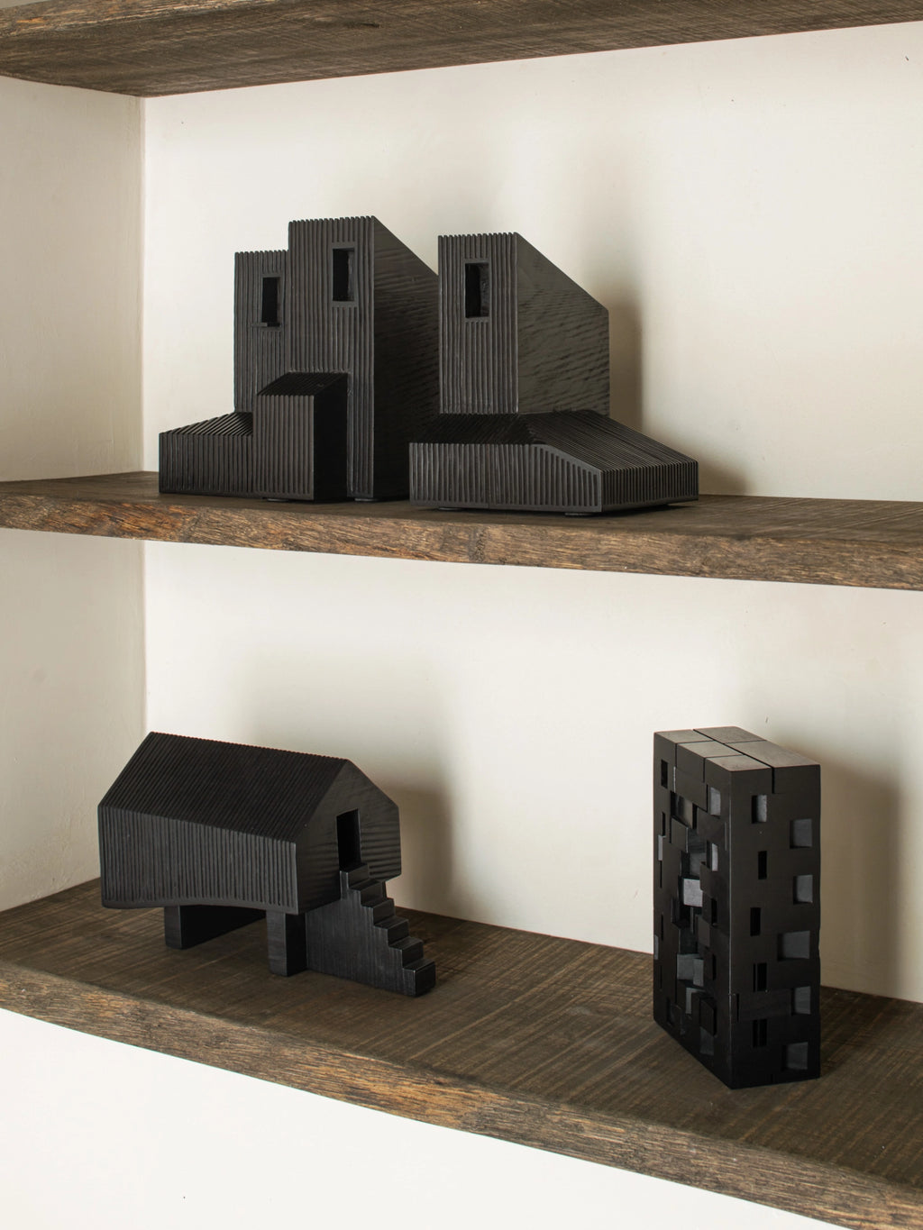 Ethnicraft Modern Farmhouse Object, a collection of three black wooden sculptures with ribbed textures, arranged on light wooden shelves. These abstract, architectural pieces create a stylish and contemporary display.